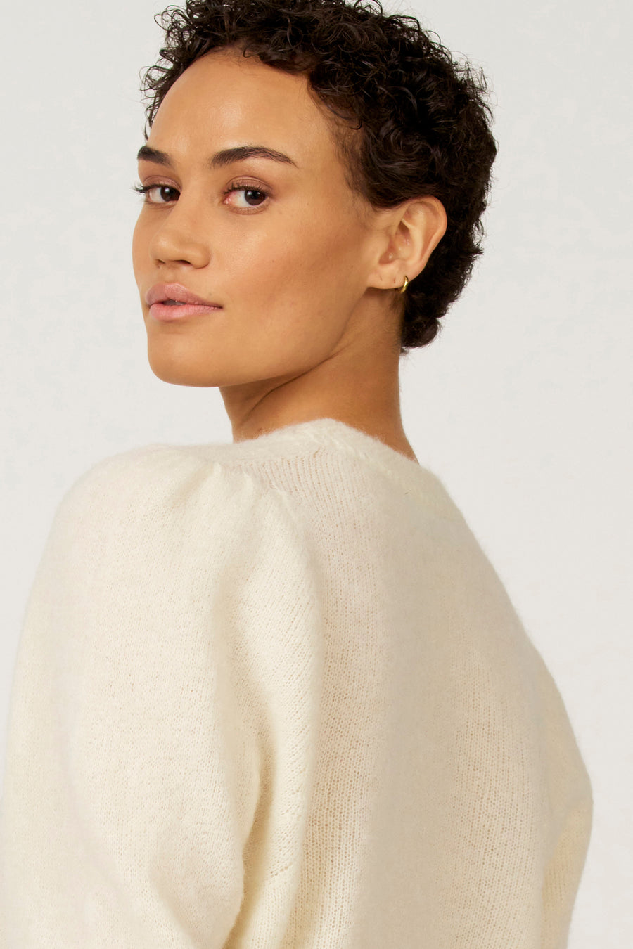 Vrouw met een witte, zachte trui die over haar schouder kijkt.