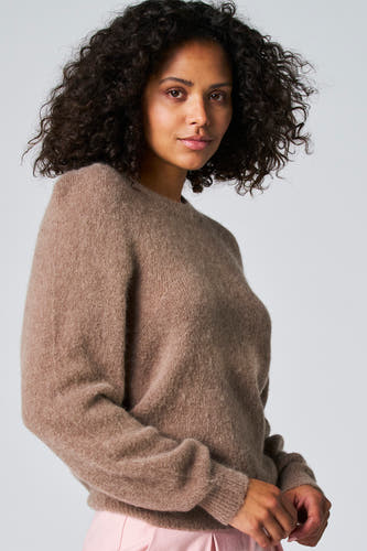 Taupekleurige trui met ronde hals van Astrid Black Label, met een zachte textuur en gedragen met een roze broek.
