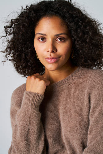 Veste taupe avec col rond d'Astrid Black Label, portée par une femme aux cheveux bouclés.