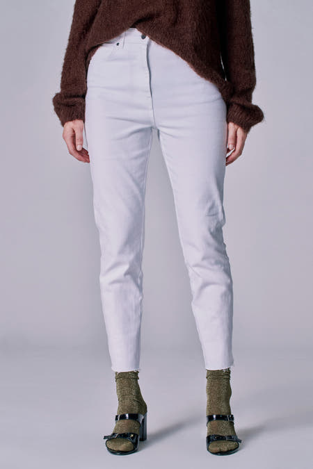 Jean blanc 7/8 d'Astrid Black Label, avec des surpiqûres en bas, associé à une chemise marron et des baskets noires avec des chaussettes dorées.