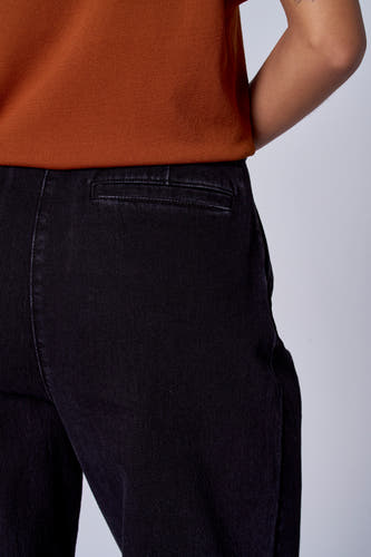 Jean délavé noir d'Astrid Black Label, avec poche arrière, associé à une chemise orange-brun.