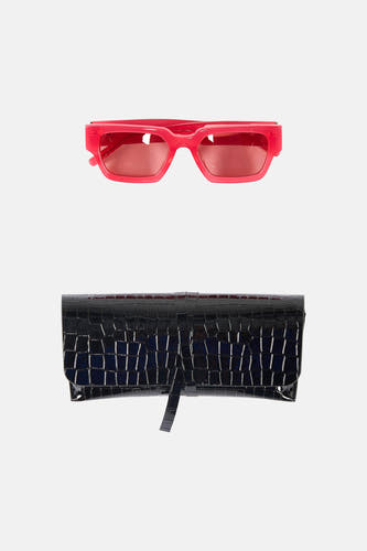 Lunettes de soleil roses Astrid Black Label, avec une pochette noire à motif crocodile en dessous, sur fond blanc.