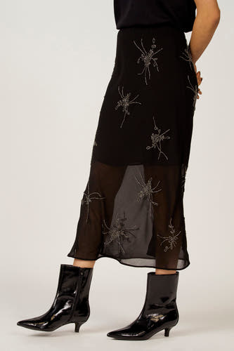 Robe noire Astrid Black Label avec des détails argentés et une transparence, associée à des escarpins noirs et brillants.