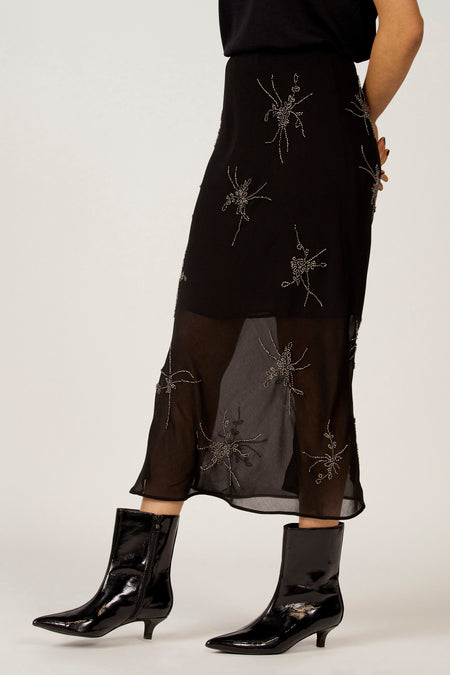 Vrouw in zwarte jurk met zilveren details en zwarte lakleren laarsjes.
