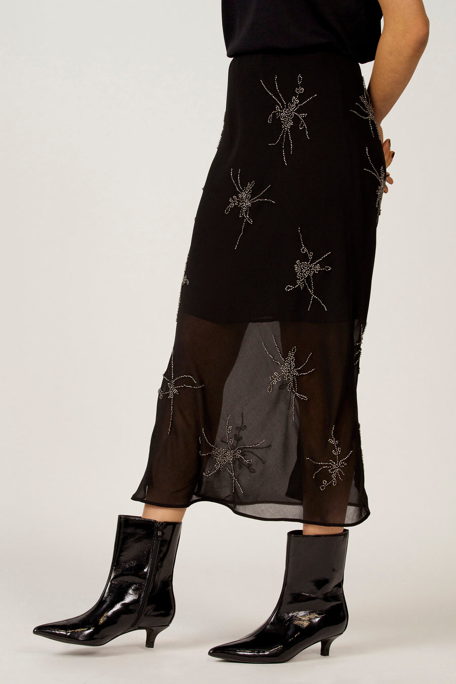 Robe noire Astrid Black Label avec des détails argentés et une transparence, associée à des escarpins noirs et brillants.