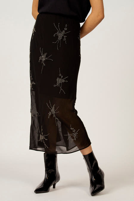 Robe noire Astrid Black Label avec des motifs floraux décoratifs en argent et une zone transparente, vue de derrière, associée à des bottines noires.