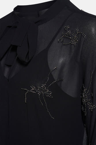 Robe noire à longues manches d'Astrid Black Label, en tissu transparent et ornée de perles.