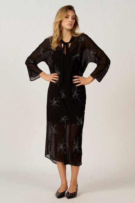 Vrouw in zwarte jurk met zilveren applicaties, staande.