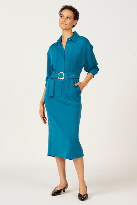 Robe bleue à longues manches d'Astrid Black Label, avec ceinture et chaussures noires.