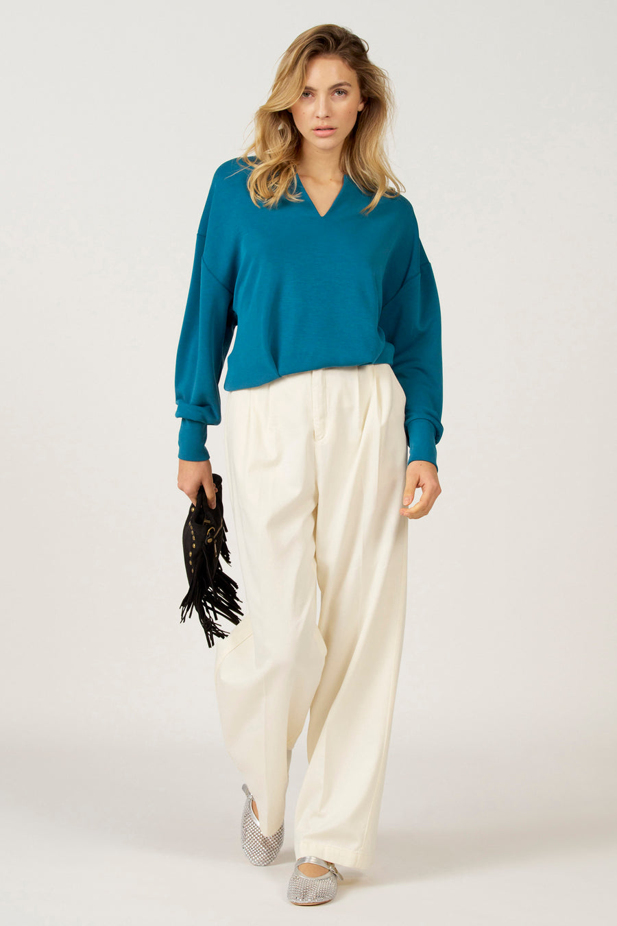 Vrouw met blauwe trui en witte broek, houdend een franjetas.