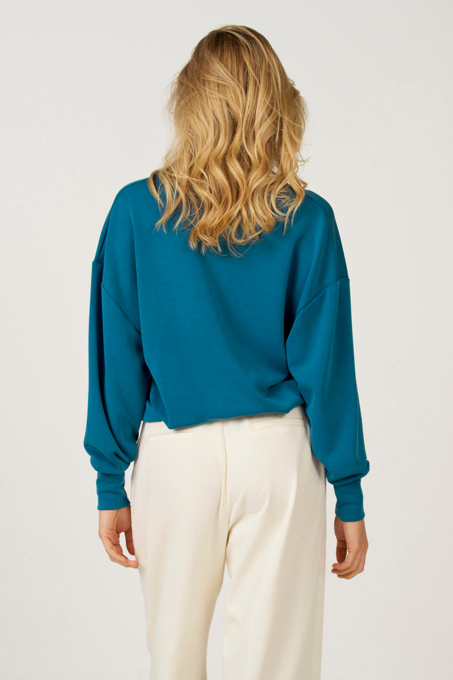 Pull bleu à col V d'Astrid Black Label, avec des manches longues et associé à un pantalon crème.