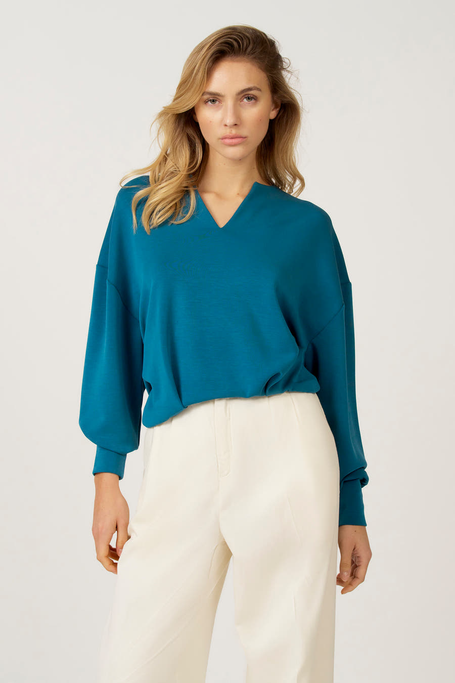 Pull bleu à col V d'Astrid Black Label, avec des manches longues et associé à une jupe blanche.