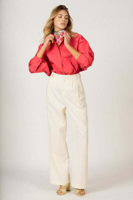 Vrouw in rode blouse, witte broek en gele sandalen.