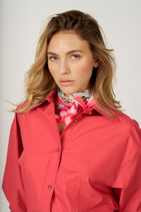 Vrouw met blond haar, roze blouse en bloemen sjaal.
