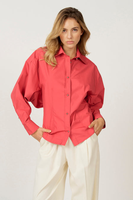 Vrouw met rode blouse en crèmekleurige broek, staand.