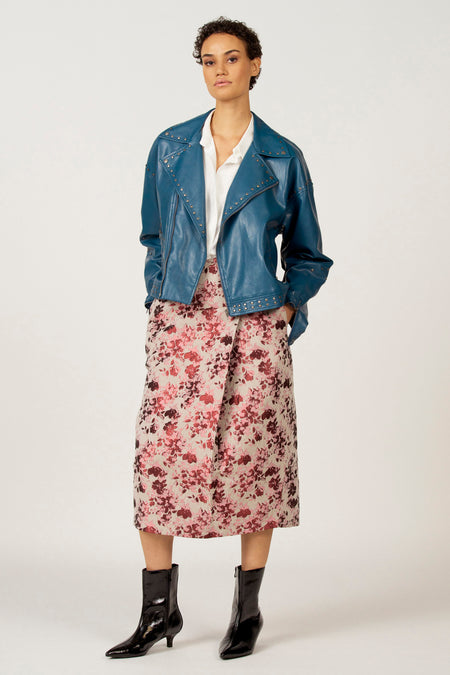 Vrouw met blauw leren jasje, bloemenrok en zwarte laarsjes.