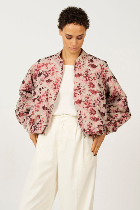 Vrouw met een bloemenjas en witte broek staat tegen een witte achtergrond.