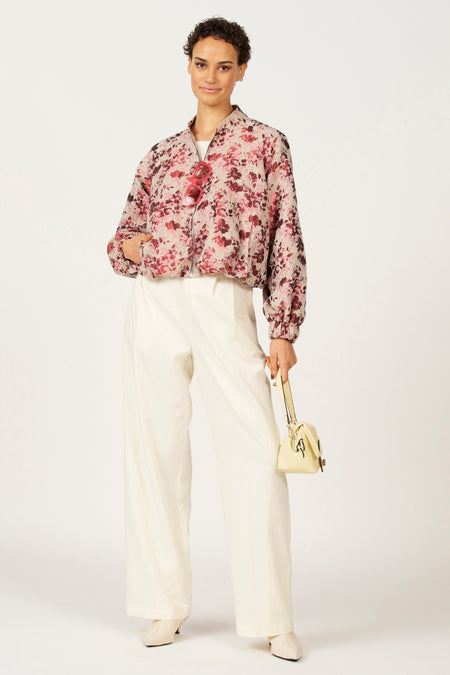 Vrouw in bloemenjas en wijde witte broek, staand met handtas.