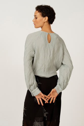 Blouse bleue à longues manches d'Astrid Black Label, avec une subtile structure plissée et un détail de nœud à l'arrière.