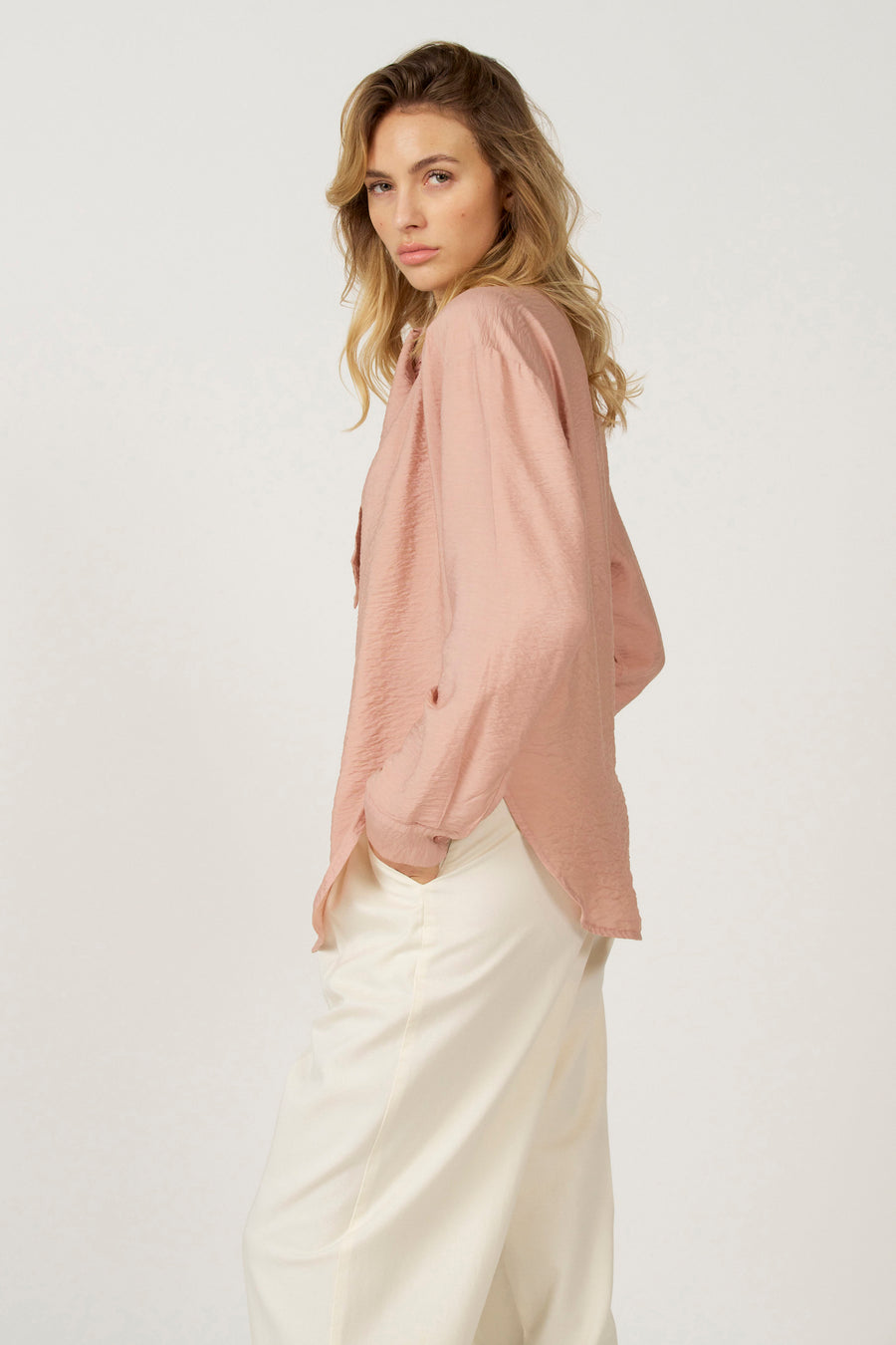 Roze blouse met lange mouwen van Astrid Black Label, met crêpe textuur en gedragen met witte broek.
