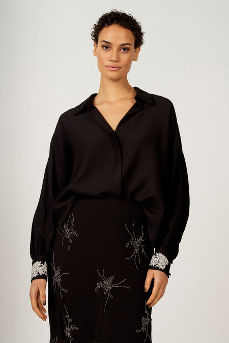 Chemise noire à longues manches d'Astrid Black Label, avec des détails argentés sur la jupe et les cols.