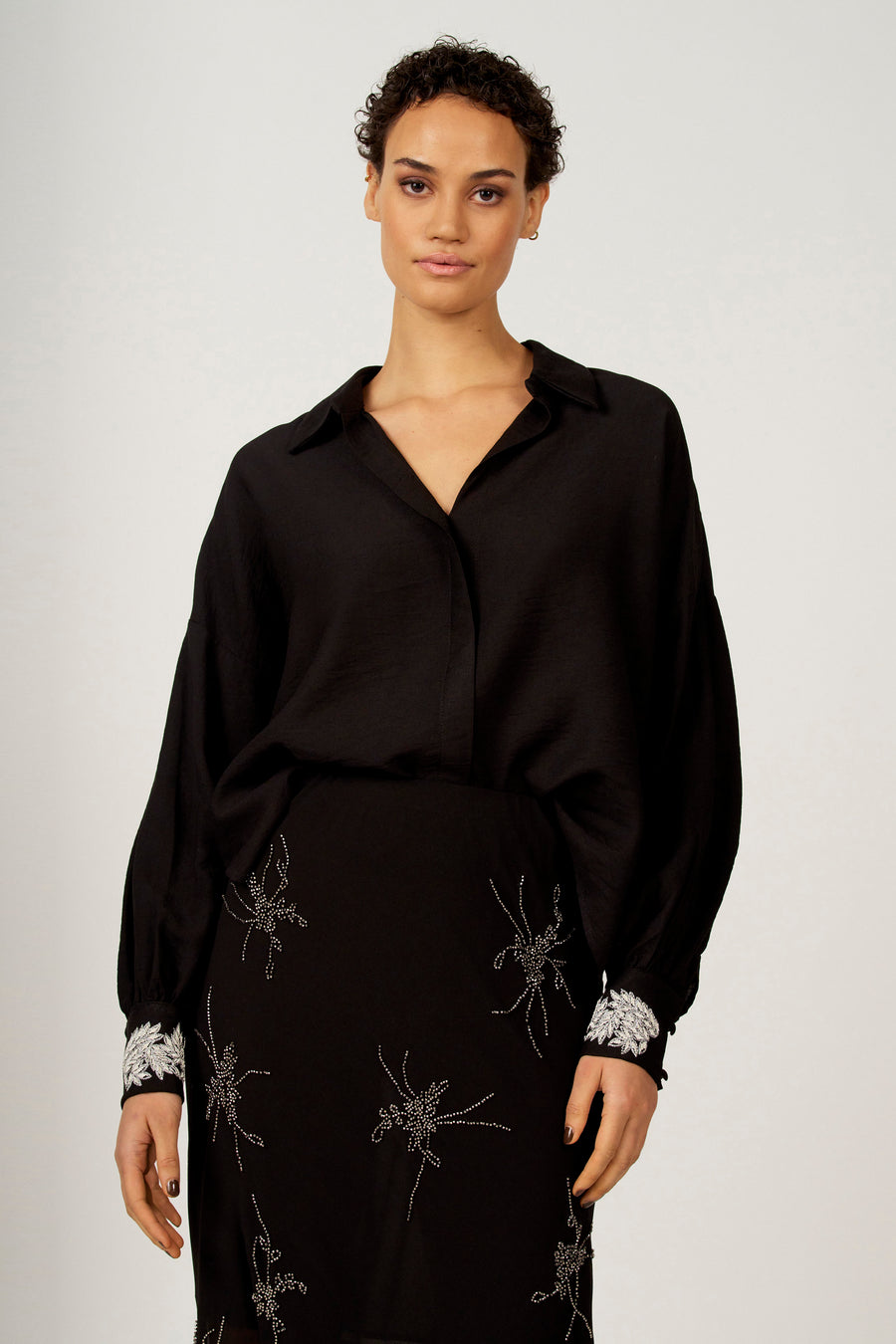 Chemise noire à longues manches d'Astrid Black Label, avec des détails argentés sur la jupe et les cols.