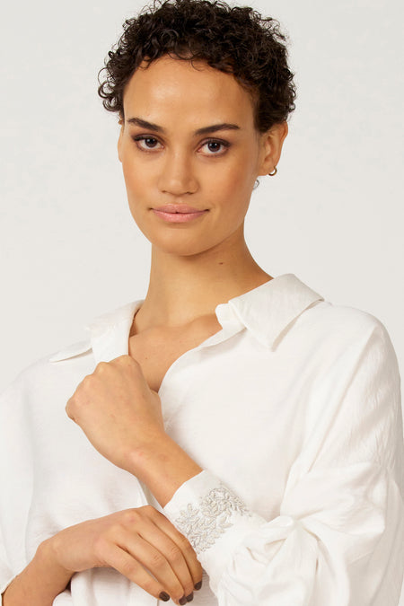 Vrouw in witte linnen blouse met geborduurde mouwen.