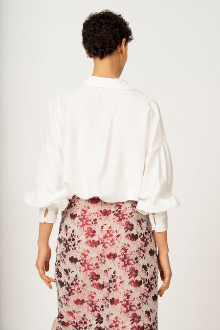 Achterkant van een vrouw in een witte blouse en een roze bloemenrok.