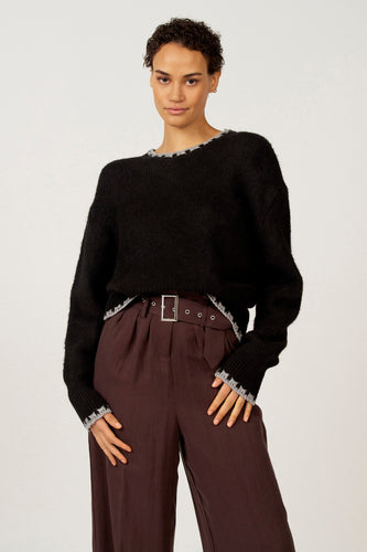 Vrouw in zwarte trui en bruine pantalon met riem.