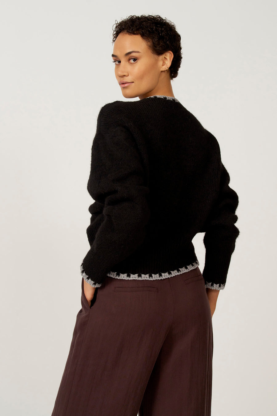 Model met zwarte trui en bruine broek.