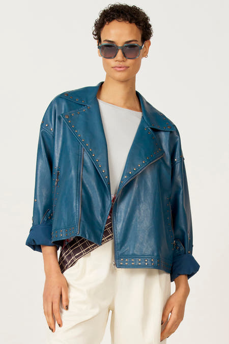 Manteau de cuir bleu Astrid Black Label, avec des strass, associé à une jupe blanche.