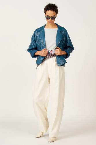 Manteau de cuir bleu d'Astrid Black Label, avec des strass argentés et une coupe décontractée, associé à un pantalon crème.