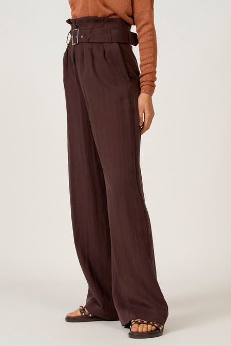 Pantalon de costume marron d'Astrid Black Label, avec une ceinture haute et des jambes larges, porté avec des sandales marrons.