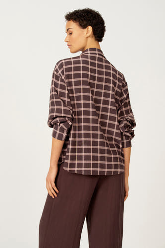 Bruine blouse met lange mouwen van Astrid Black Label, met roze ruitpatroon, gedragen met een bruine broek.
