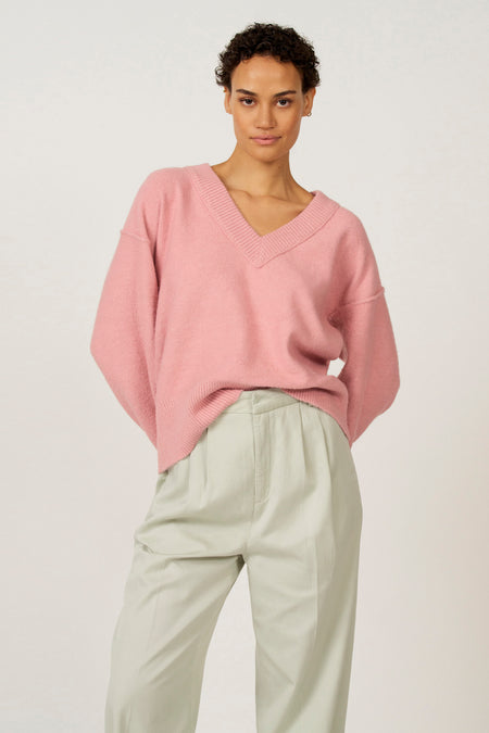 Vrouw in roze trui en groene pantalon.