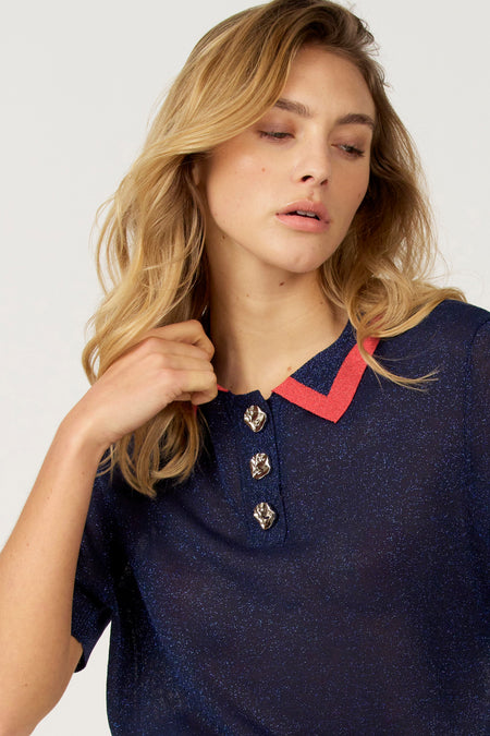 Vrouw draagt fonkelende marineblauwe polo met rode kraag en decoratieve knopen.