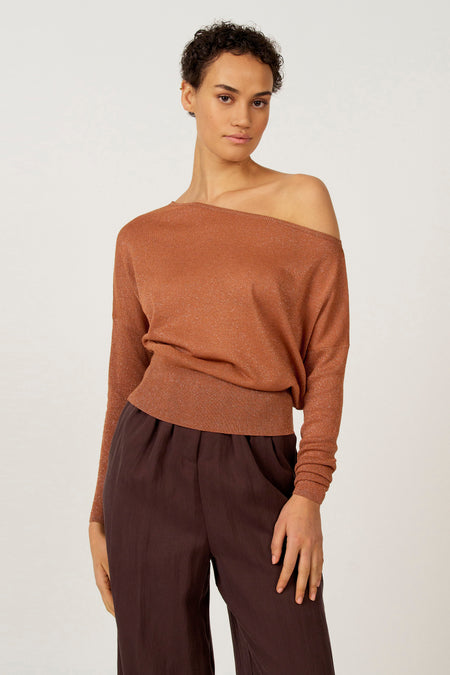 Vrouw in koperkleurige trui met bruine broek, staand.