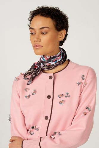 Gilet rose d'Astrid Black Label, orné de paillettes argentées à motif floral, associé à un foulard en soie dessiné.