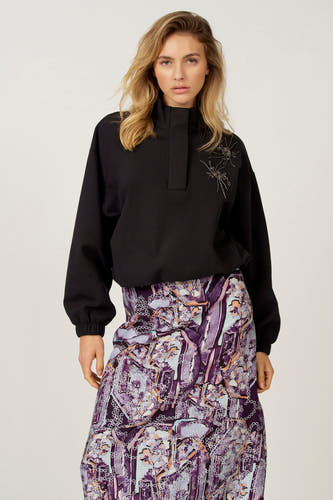 Pull noir Astrid Black Label, à manches longues et col montant, combiné avec une jupe à imprimé floral.