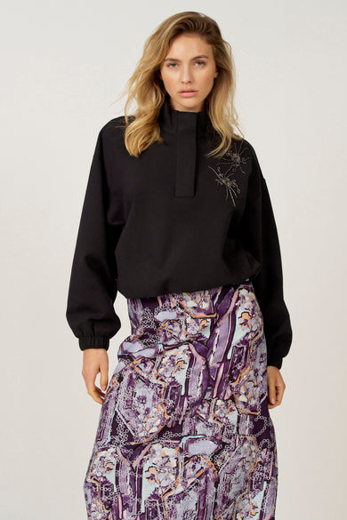 Pull noir Astrid Black Label, à manches longues et col montant, combiné avec une jupe à imprimé floral.