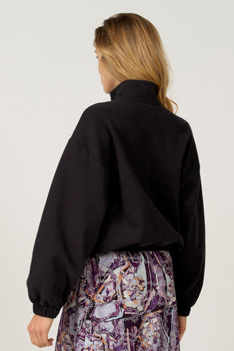 Zwarte sweater van Astrid Black Label, met lange mouwen en een hoge kraag, gecombineerd met een rok met bloemenprint.