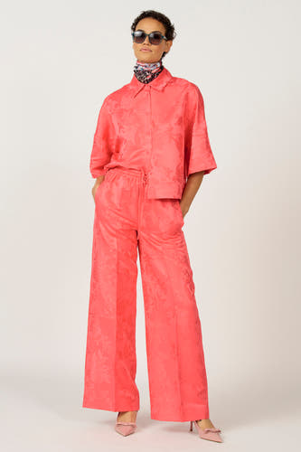 Blouse rose d'Astrid Black Label, avec motif floral et portée avec un pantalon coordonné et des lunettes de soleil.