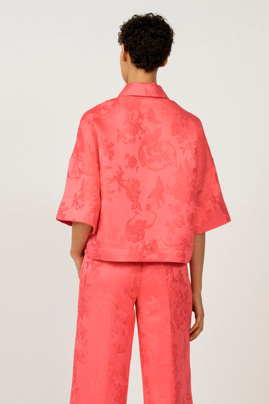 Achterkant van een model in een roze, gebloemde broek en blouse.