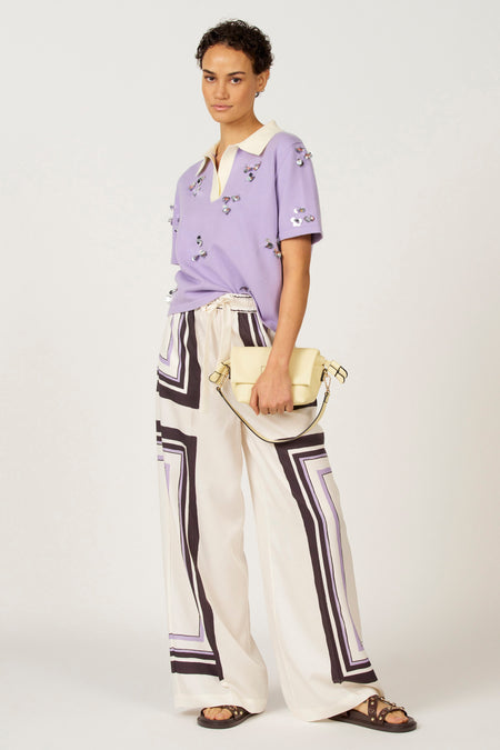 Polo noire à manches courtes d'Astrid Black Label, ornée de paillettes argentées, associée à un short blanc avec un motif géométrique et des sandales.