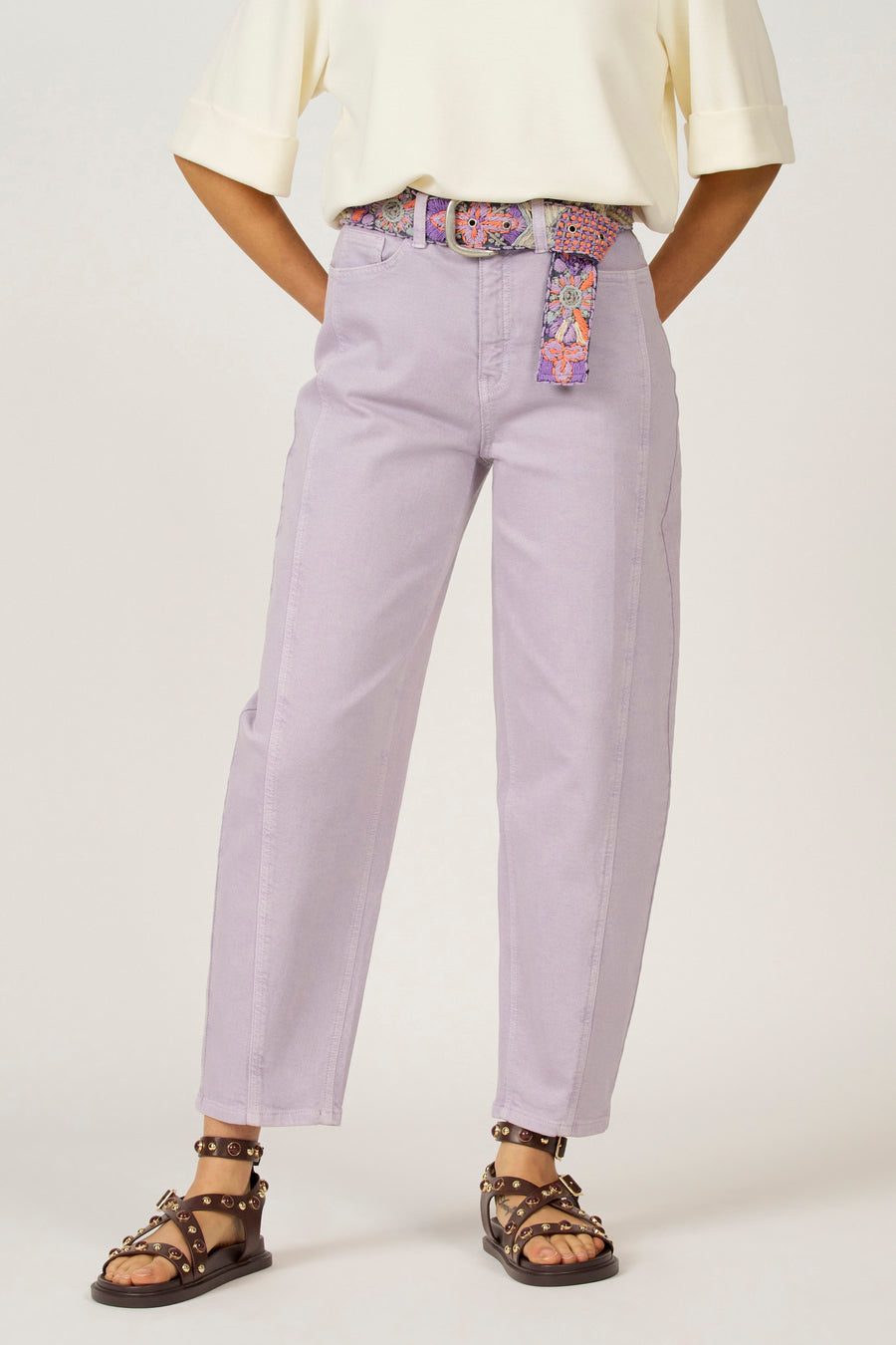 Paarse jeans met geborduurde riem, bruine sandalen.
