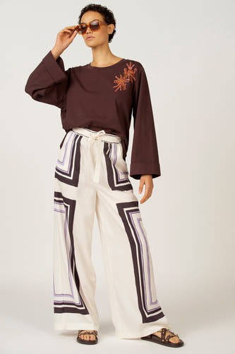 Pantalon multicolore Astrid Black Label, avec imprimé géométrique noir et lilas, combiné avec des sandales tressées et un sac jaune.
