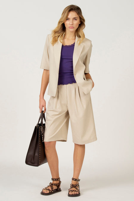 Vrouw met beige blazer en culottes, paarse top, bruine tas en sandalen.