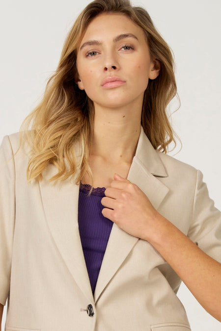 Vrouw in beige blazer en paarse top.