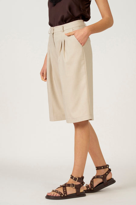 Model in bruine top, beige shorts en bruine sandalen.
