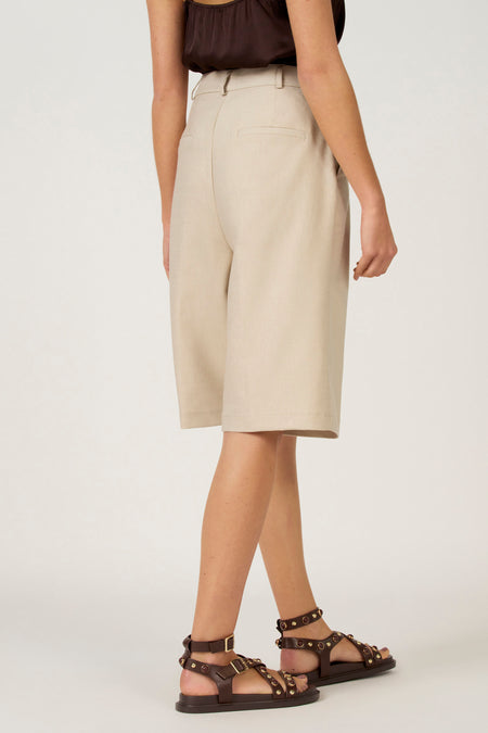 Model met beige bermuda en bruine sandalen.